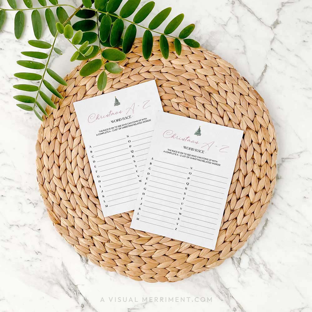 2 modern christmas A-Z word race game cards on a woven placemat with green leaves