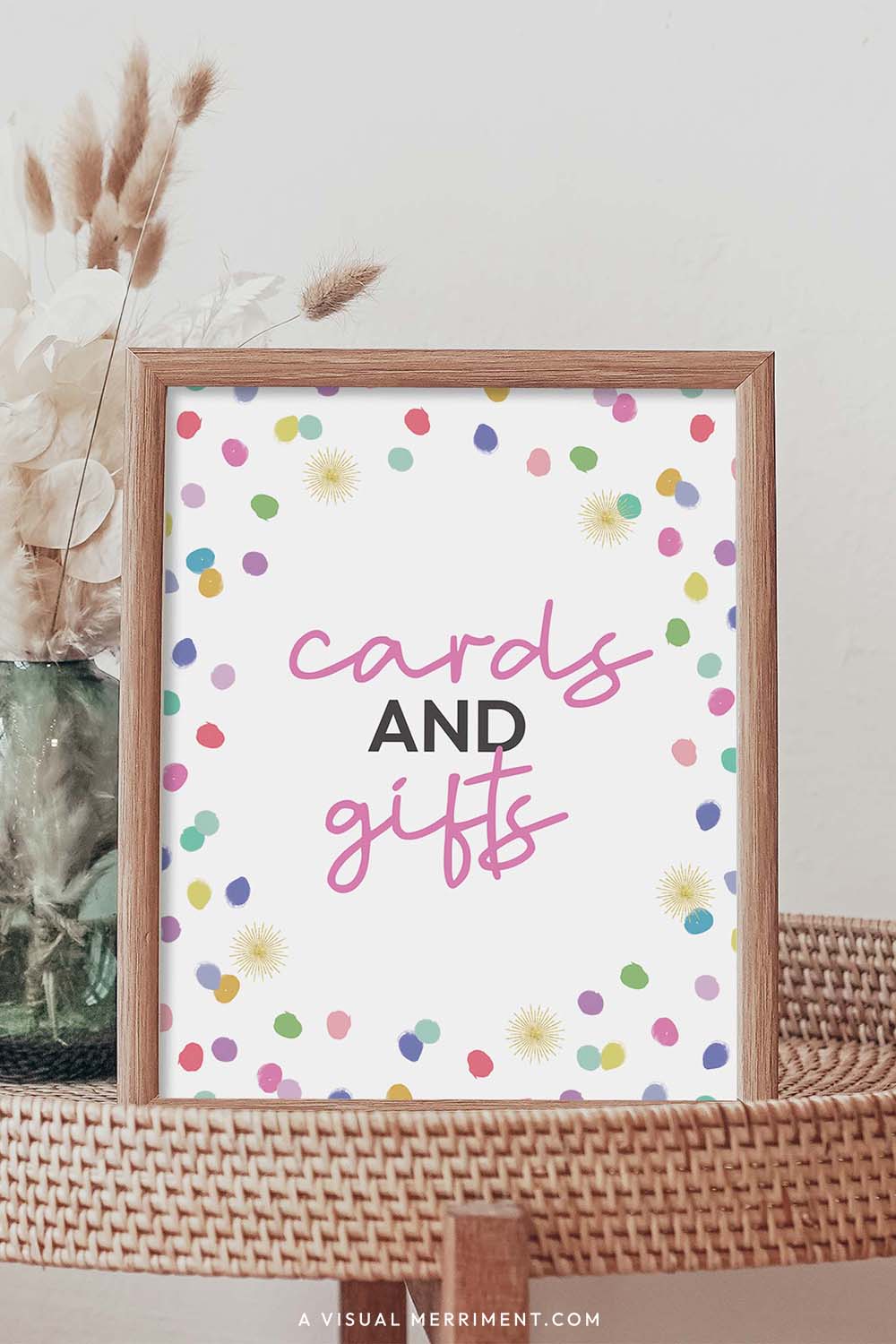 cards and gifts rainbow confetti polka dot printable party sign in a frame sitting on a grass table with a vase of boho stems