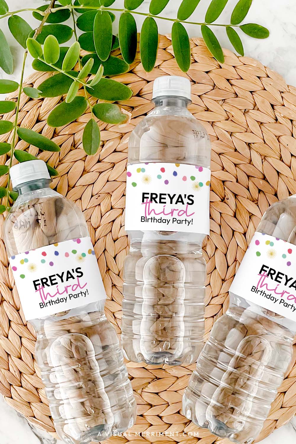 Vertical of bottles with rainbow confetti water bottle labels in polka dot design on grass mat with leaves