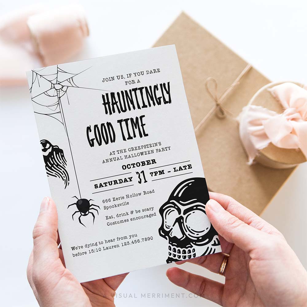 A person holds a Halloween invitation card with spooky black line art and text, with a kraft gift box and pink ribbon in the background.