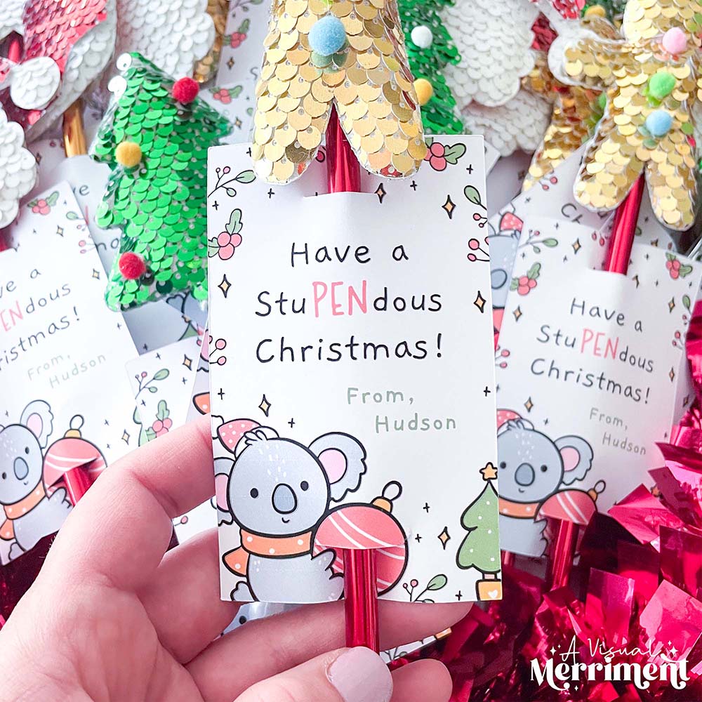 hand holding christmas pen wrapped in printable gift tag with other pens in background