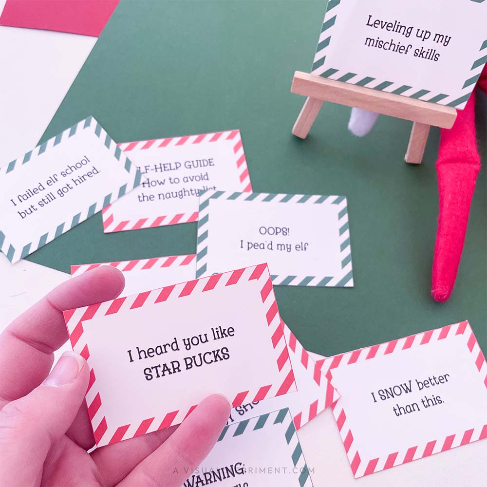 hand holding red funny elf on the shelf idea sign with other signs scattered