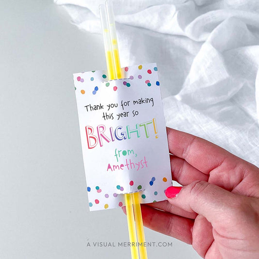Hand holding 'thank you for making this year bright' glow stick holder with sticks in colorful rainbow confetti polka dot design