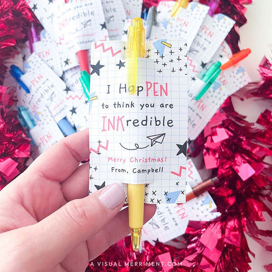 hand holding pen with christmas gift tag printable and tinsel in background