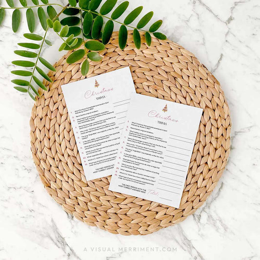2 modern christmas trivia game cards on a woven placemat with green leaves