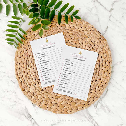 2 modern christmas word scramble cards on a woven placemat with green leaves