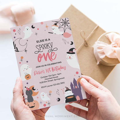 hands holding pink spooky one birthday invitation with ghosts, pumpkins, stars in a celestial design