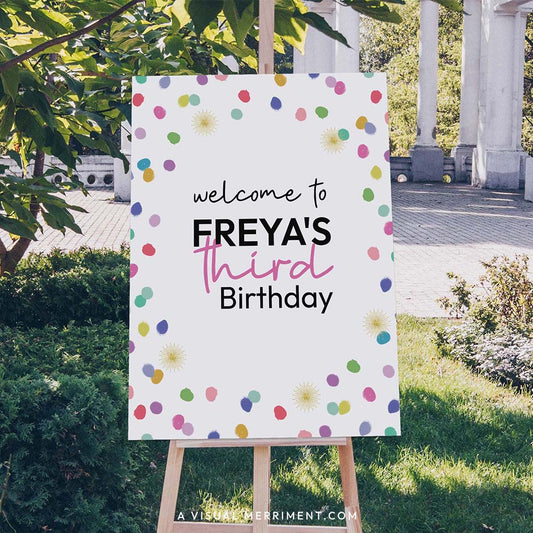 Large custom welcome sign with colorful rainbow confetti polka dots on an easel outdoors.