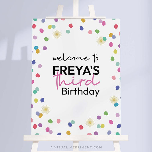Large colorful welcome birthday sign with rainbow confetti polka dots on a white easel