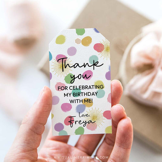 Hand holding colorful rainbow confetti party favor gift tag with polka dots
