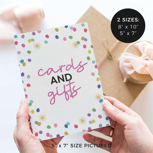 hands holding ‘cards and gifts’ birthday party sign with rainbow confetti polka dot design and gifts in background