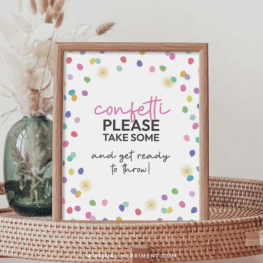 Please take confetti rainbow polka dot printable party sign in a frame sitting on a grass table with a vase of boho stems