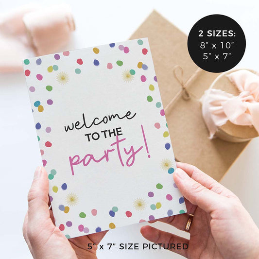 hands holding ‘welcome to the party’ wedding sign with rainbow confetti polka dot design and gifts in background