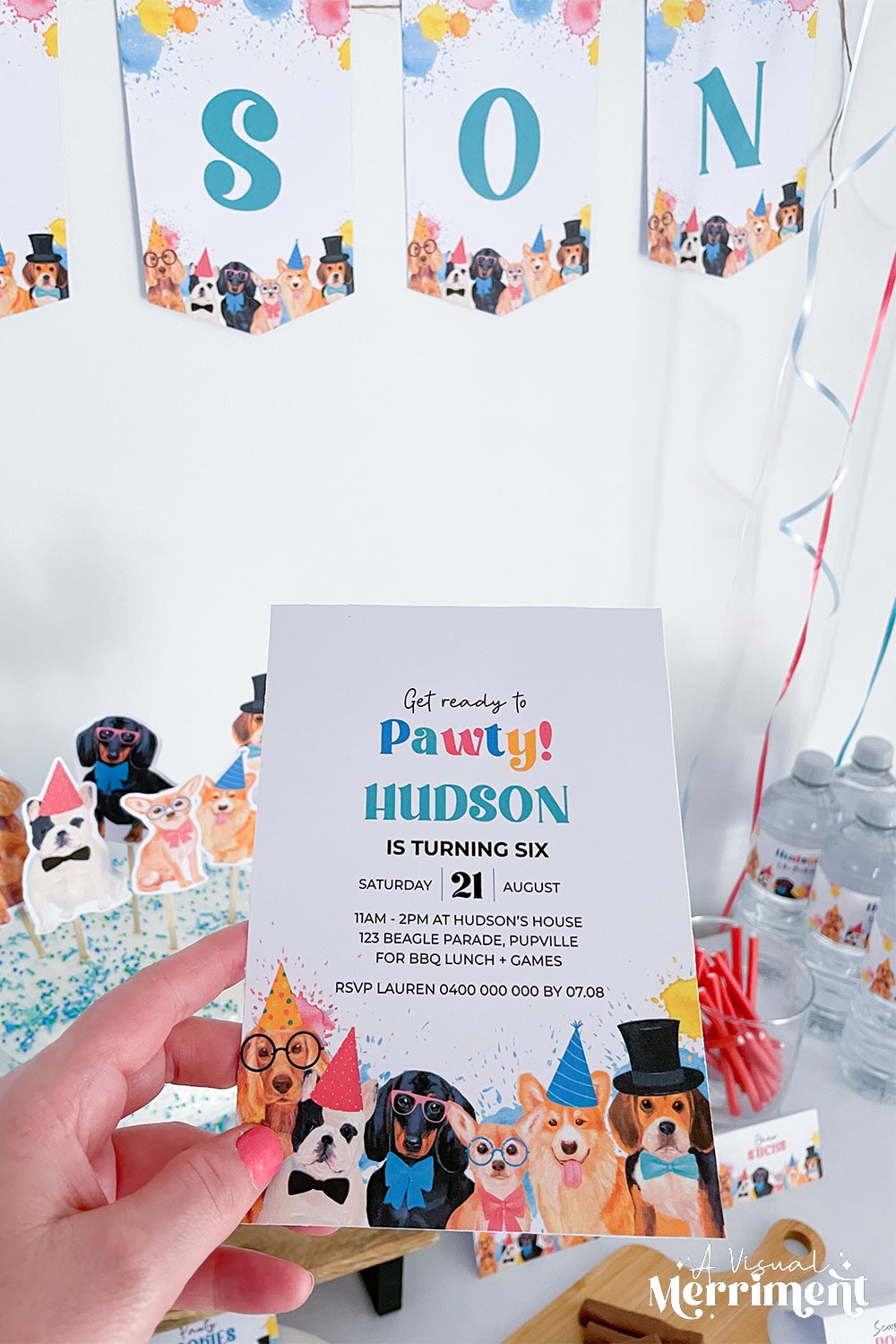 hand holding pawty dogs invitation with party decorations and treats in background
