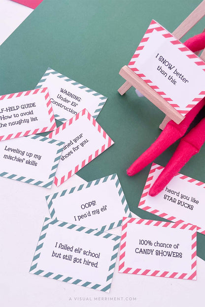 Vertical of red and green funny elf on the shelf ideas signs on easel next to elf doll