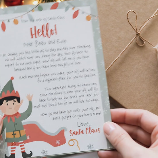 video of hands showing christmas elf printed letter with gifts in background