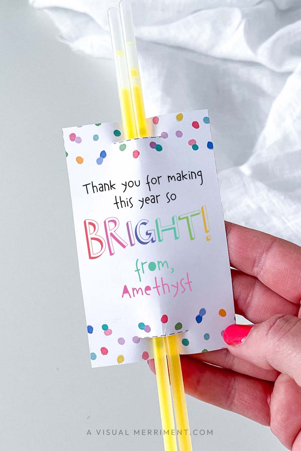 vertical of Hand holding 'thank you for making this year bright' glow stick holder with sticks in colorful rainbow confetti polka dot design