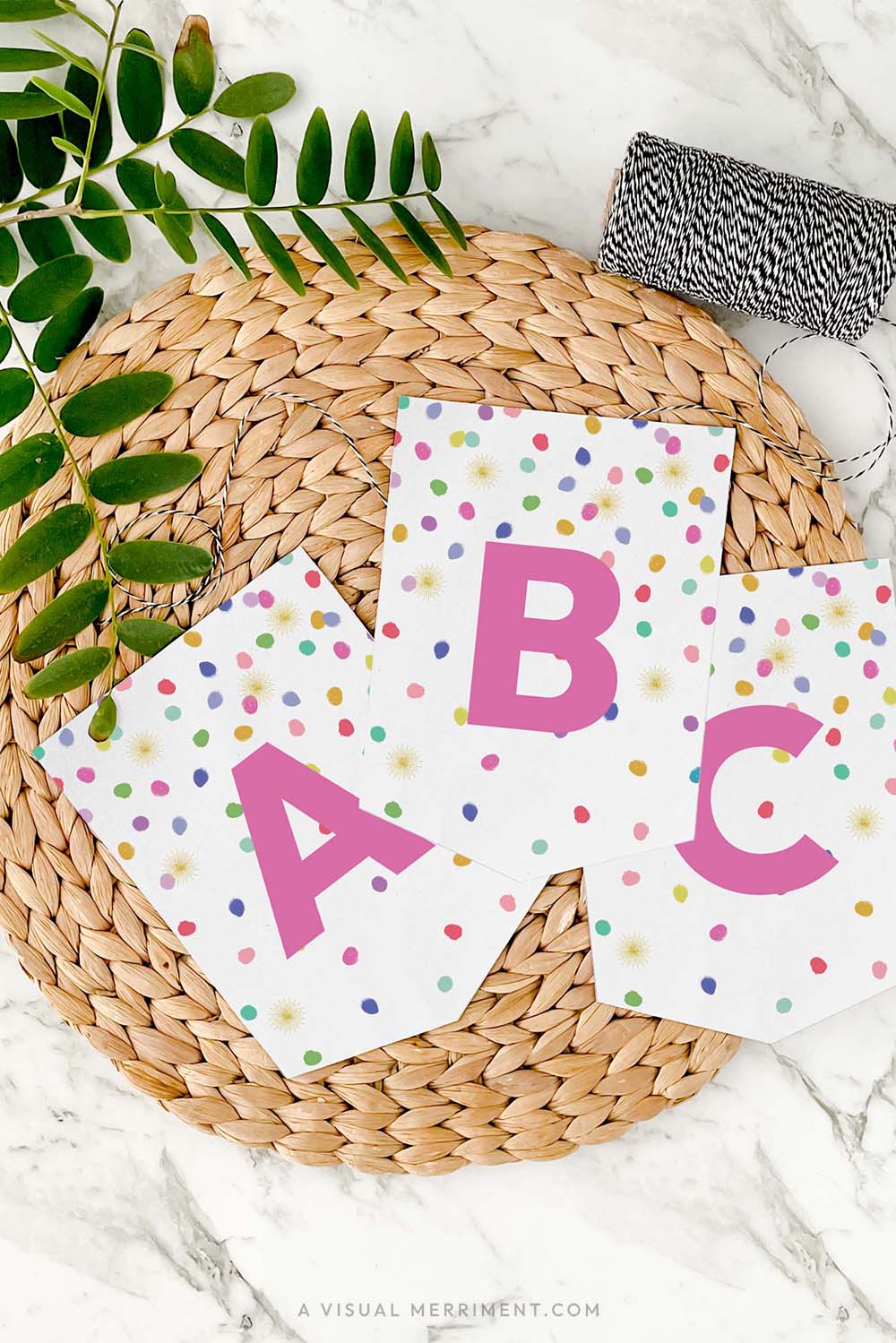 set of 3 letter banner flags in colorful rainbow confetti design on mat with twine and leaves