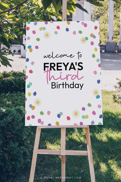 Vertical Large custom welcome sign with colorful rainbow confetti polka dots on an easel outdoors.